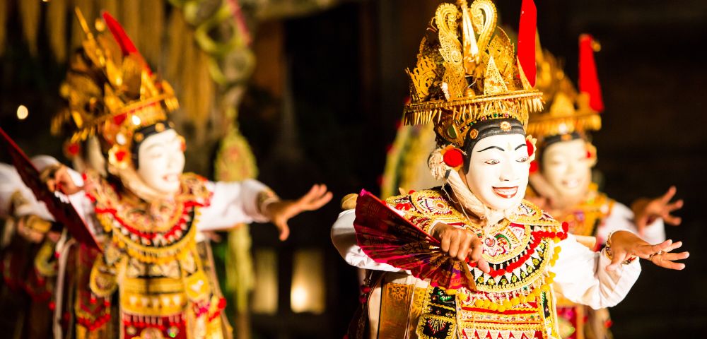 Three Balinese dancers in traditional costumes and ornate headdresses perform a vibrant dance.