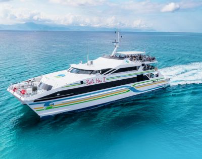 A sleek white ferry with colorful stripes sails on clear blue ocean waters under a partially cloudy sky, conveying a sense of serenity and adventure.