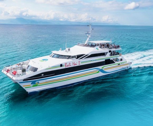 A sleek white ferry with colorful stripes sails on clear blue ocean waters under a partially cloudy sky, conveying a sense of serenity and adventure.