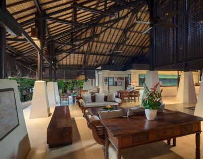 Spacious living area with high, vaulted ceiling and wooden beams. Features elegant furniture, tropical plants, and a warm, inviting ambiance.