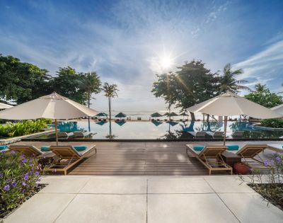 Luxurious poolside scene at sunrise with lounge chairs and umbrellas, overlooking a tranquil infinity pool, lush greenery, and a calm ocean horizon.