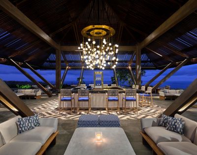 Spacious lounge with modern decor at dusk, featuring cozy seating, a central bar, and an elegant chandelier, creating a warm, inviting atmosphere.