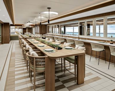 Stylish, modern restaurant interior with a long wooden communal table set with plates, surrounded by cushioned chairs. Large windows reveal a scenic view.