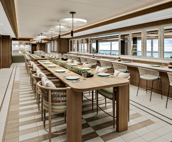 Stylish, modern restaurant interior with a long wooden communal table set with plates, surrounded by cushioned chairs. Large windows reveal a scenic view.