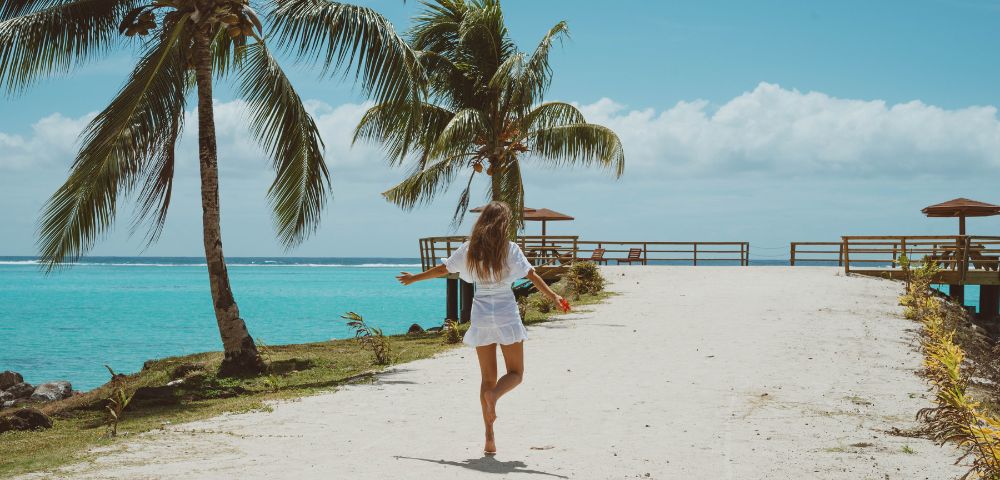 A woman walks on the beach with her arms outstretched, enjoying the sun and sea breeze.