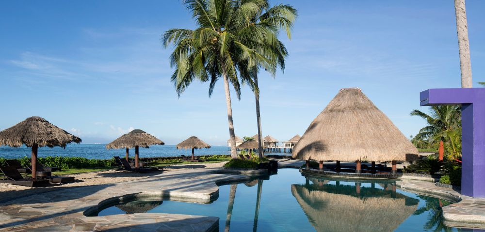 A serene pool surrounded by thatched umbrellas and swaying palm trees, perfect for relaxation and tropical vibes.