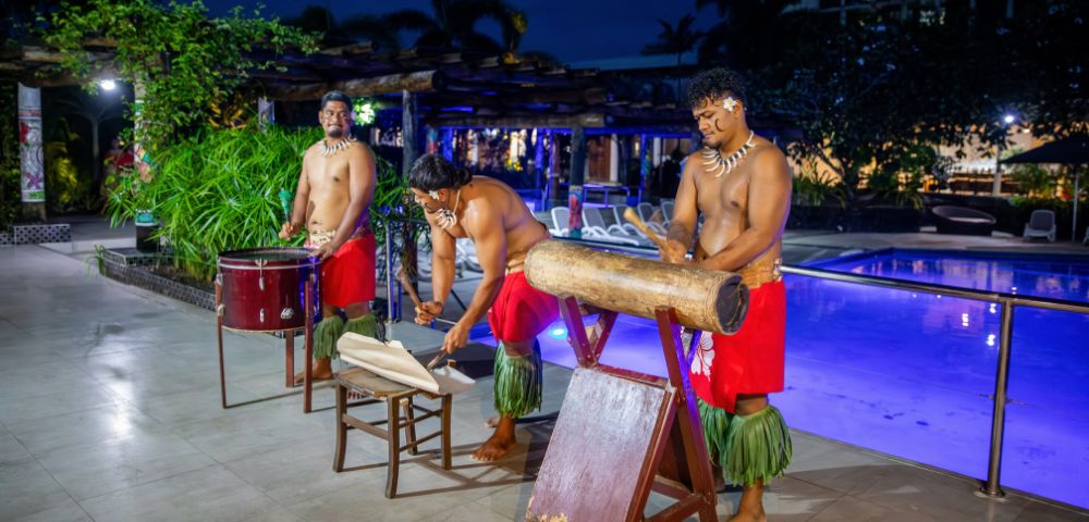 Three men in matching red outfits play drums by a pool, creating a lively atmosphere.