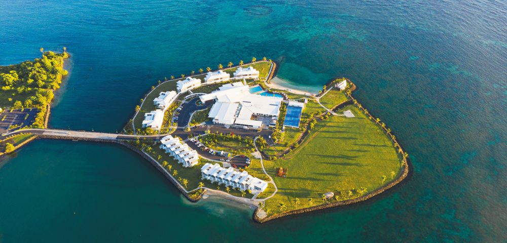 Aerial view of a tropical island resort surrounded by clear blue water and lush greenery.