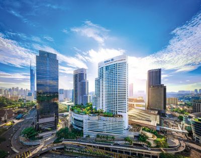 Aerial view of modern cityscape with tall skyscrapers under a bright blue sky. Sunlight breaks through clouds, creating a vibrant and dynamic urban atmosphere.