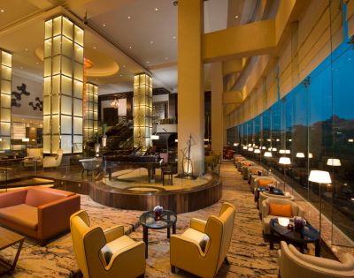 Luxurious hotel lounge with modern seating, large glowing pillars, and floor-to-ceiling windows, creating an elegant, inviting ambiance at dusk.