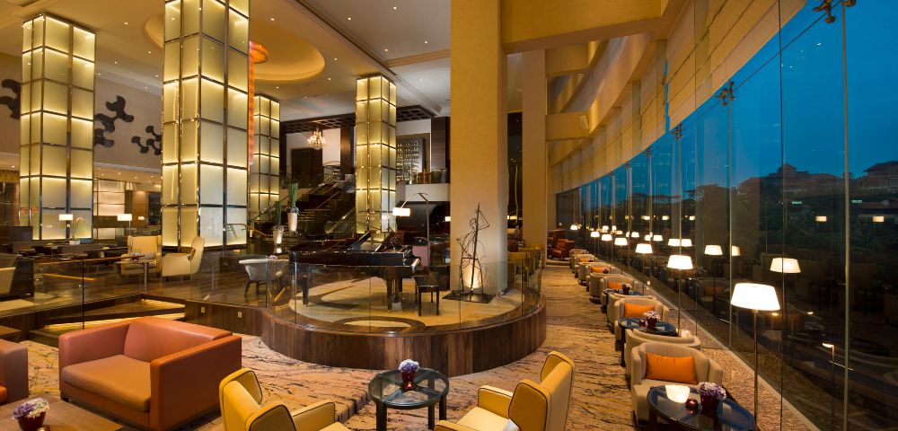 Luxurious hotel lounge with modern seating, large glowing pillars, and floor-to-ceiling windows, creating an elegant, inviting ambiance at dusk.