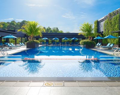 Luxurious outdoor pool with clear blue water, surrounded by lounge chairs and blue umbrellas. Palm trees and greenery create a tropical, relaxing atmosphere.