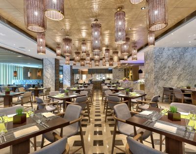 Modern restaurant interior with elegant lighting fixtures, patterned floor, and neatly arranged tables set for dining, creating a sophisticated ambiance.
