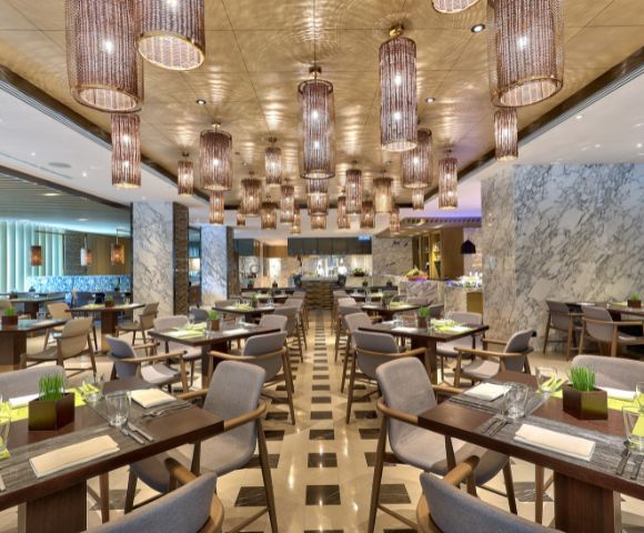 Modern restaurant interior with elegant lighting fixtures, patterned floor, and neatly arranged tables set for dining, creating a sophisticated ambiance.