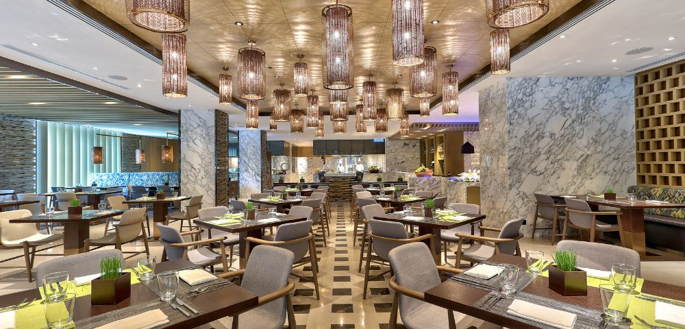 Modern restaurant interior with elegant lighting fixtures, patterned floor, and neatly arranged tables set for dining, creating a sophisticated ambiance.