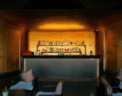 Sophisticated bar interior with dim lighting, warm golden hues, a stocked shelf of bottles, and cozy seating with plush pillows, creating an inviting ambiance.