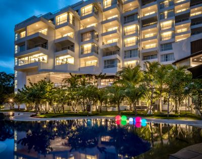 Illuminated hotel building at night with warm lights, a reflective pool in the foreground, surrounded by palm trees, and glowing colorful spheres.