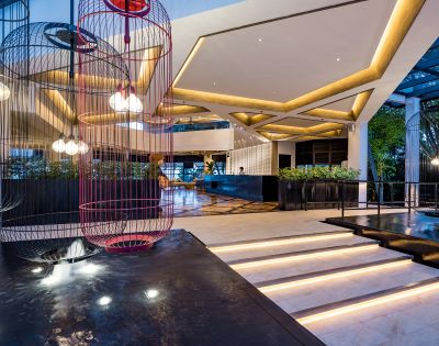 Spacious modern hotel lobby with geometric lighting, two large birdcage light fixtures, sleek white marble steps, and greenery, exuding elegance and warmth.