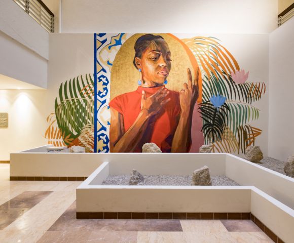 A vibrant mural depicts a thoughtful woman in a red shirt, surrounded by abstract leaves and geometric patterns. The scene is situated in a modern, serene atrium.