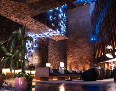 Modern lounge with textured brick walls, soft ambient blue lighting, and cozy seating. Indoor plants add a touch of nature. Relaxed, elegant atmosphere.