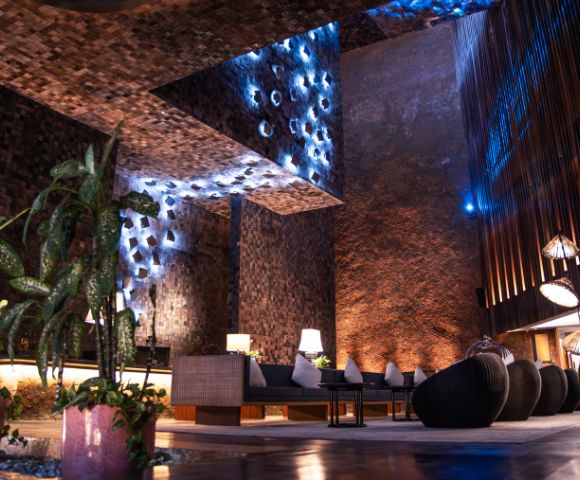 Modern lounge with textured brick walls, soft ambient blue lighting, and cozy seating. Indoor plants add a touch of nature. Relaxed, elegant atmosphere.