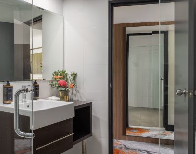 Modern bathroom with clean lines featuring a white sink, dark wood accents, and a large mirror. Bright flowers add a touch of color and freshness.