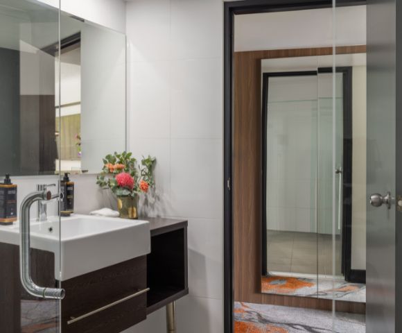 Modern bathroom with clean lines featuring a white sink, dark wood accents, and a large mirror. Bright flowers add a touch of color and freshness.
