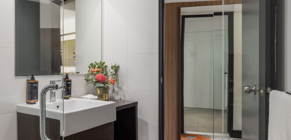 Modern bathroom with clean lines featuring a white sink, dark wood accents, and a large mirror. Bright flowers add a touch of color and freshness.