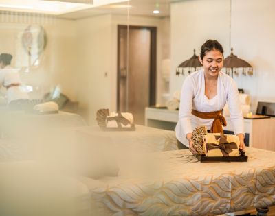 A smiling woman arranges towels on a massage table in a serene spa room, conveying a calm and welcoming atmosphere.