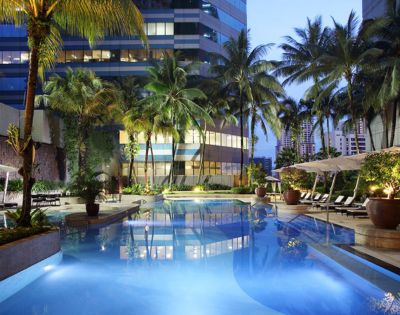 Luxurious hotel pool at twilight surrounded by palm trees and modern high-rise buildings. Lounge chairs and umbrellas create a serene, inviting atmosphere.