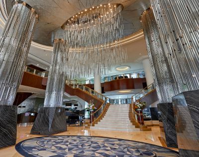 Luxurious hotel lobby featuring grand marble pillars, a dramatic spiral staircase, and an intricate circular chandelier, exuding elegance and sophistication.