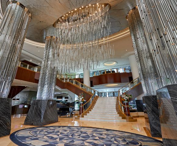 Luxurious hotel lobby featuring grand marble pillars, a dramatic spiral staircase, and an intricate circular chandelier, exuding elegance and sophistication.