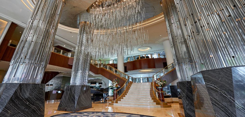 Luxurious hotel lobby featuring grand marble pillars, a dramatic spiral staircase, and an intricate circular chandelier, exuding elegance and sophistication.