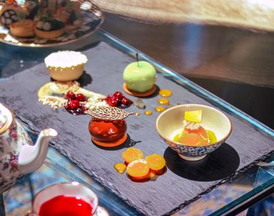 Elegant dessert assortment on a slate platter includes a green mousse sphere, a caramel tart, and decorative cherry garnishes, exuding a luxurious, gourmet vibe.