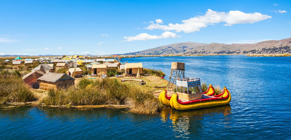 A vibrant floating island on Lake Titicaca with traditional reed huts, lush greenery, and a decorative yellow boat. The scene exudes tranquility.