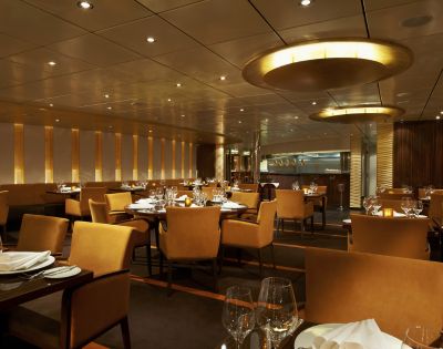 Elegant restaurant interior with warm lighting, featuring neatly arranged tables with beige chairs, pristine white tablecloths, and sparkling glassware.