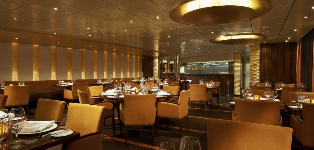 Elegant restaurant interior with warm lighting, featuring neatly arranged tables with beige chairs, pristine white tablecloths, and sparkling glassware.
