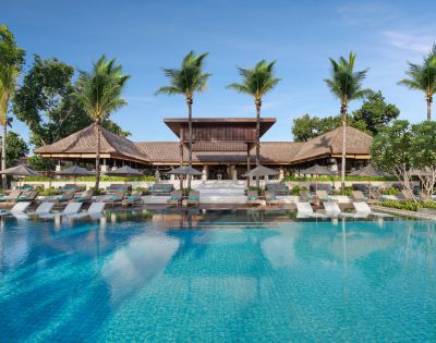 Luxurious tropical resort with a large, clear blue pool, surrounded by palm trees and wooden architecture, creating a serene and inviting atmosphere.