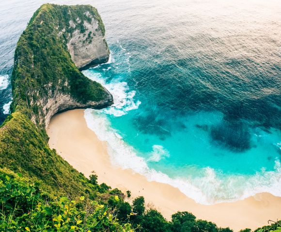 Aerial view of a pristine beach surrounded by lush cliffs and turquoise ocean waves. The scene is tranquil and inviting, evoking a sense of tropical paradise.