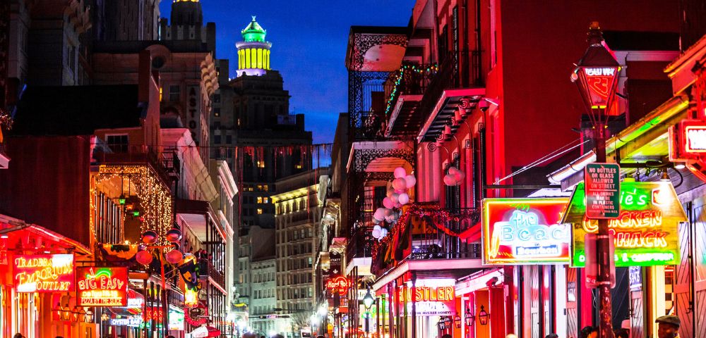 Bustling New Orleans street at night with colorful neon lights, lively crowds, and historic buildings, creating a vibrant and festive atmosphere.