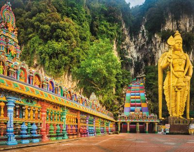 A vibrant Hindu temple with intricate, colorful carvings leads to a towering, gold statue amidst lush greenery and rocky cliffs, conveying awe and spirituality.
