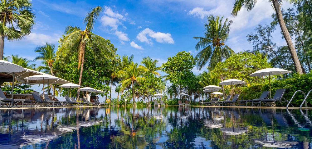 A serene tropical poolside scene with lounge chairs, umbrellas, and a swim-up bar surrounded by palm trees under a bright blue sky. Relaxing atmosphere.