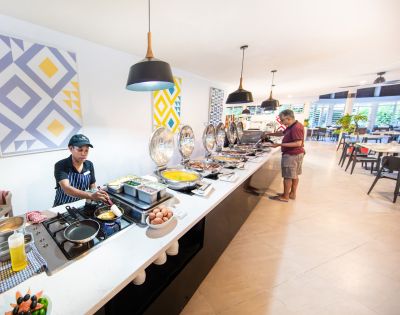 A buffet service area with a chef preparing food on a counter filled with dishes. A man is serving himself, in a bright, modern dining room.