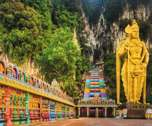Vibrant temple facade and colorful staircase lead to towering golden statue in lush, rocky landscape. Scene conveys awe and cultural richness.