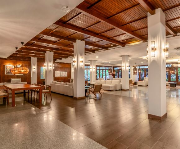Spacious hotel lobby with warm lighting, wooden ceiling, and sleek pillars. Contemporary furniture and large windows create an inviting atmosphere.