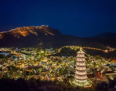 Illuminated mountain town at night with a pagoda in the foreground, glowing buildings, and mountains in the background. The atmosphere is serene and picturesque.