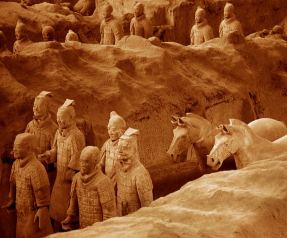 Ancient Terracotta Army sculptures in an excavation pit; lifelike clay warriors and horses, aligned in rows. The scene conveys historical depth and solemnity.