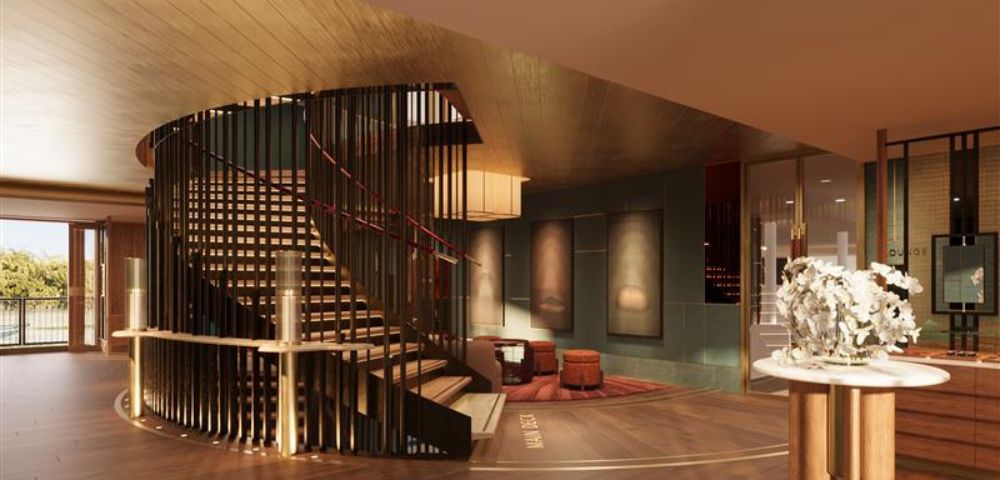 Luxurious hotel lobby with a spiral staircase, warm lighting, modern art on walls, and plush seating. The ambiance is elegant and inviting.