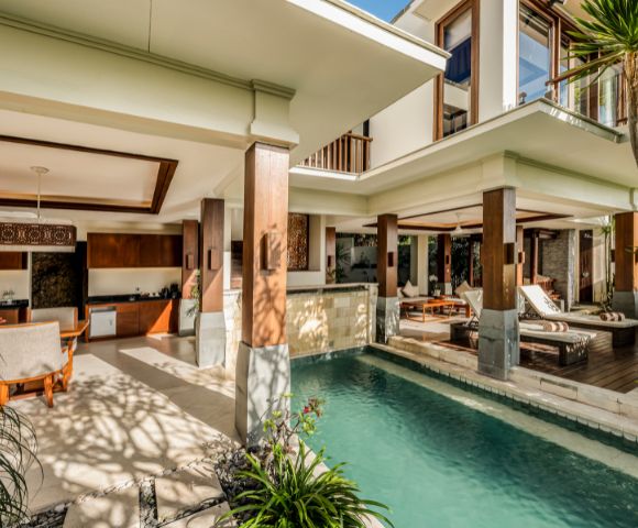Luxurious open-concept villa with a modern design, featuring a stylish living area, lush pool, wooden accents, and tropical plants, creating a serene atmosphere.