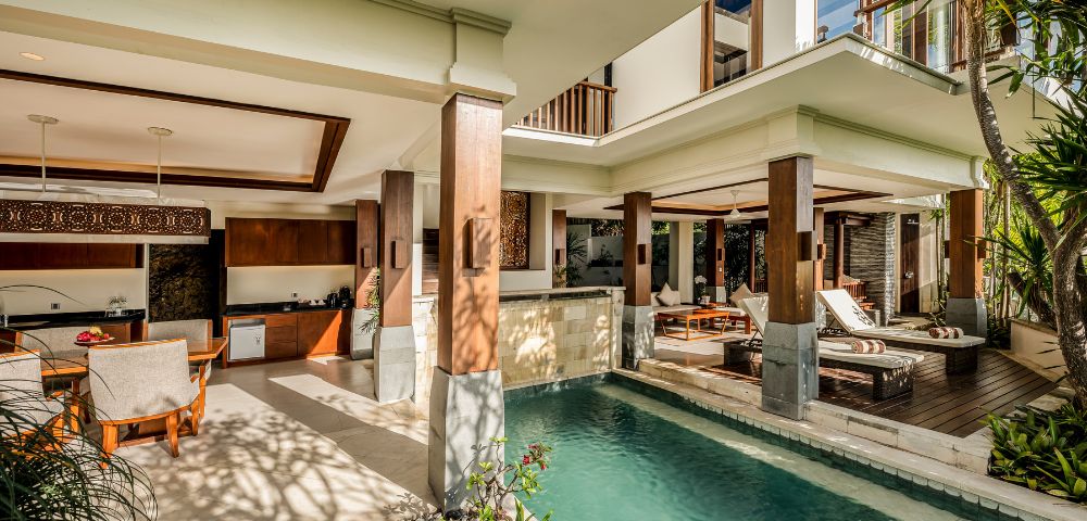 Luxurious open-concept villa with a modern design, featuring a stylish living area, lush pool, wooden accents, and tropical plants, creating a serene atmosphere.